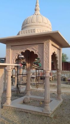 an ornately decorated gazebo in the middle of a dirt area with chairs around it