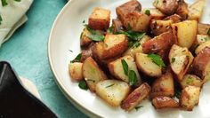 a white plate topped with potatoes and parsley on top of a blue table cloth