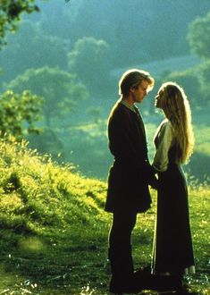 a man and woman standing next to each other in front of a tree filled field