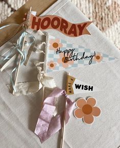 a birthday card and some paper flowers on top of a piece of cloth with the words hooray written on it