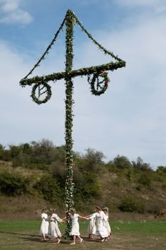 three girls in white dresses are standing around a cross made out of flowers and ribbons