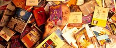 there are many books stacked on top of each other in this pile and one person is holding his hand up to the book