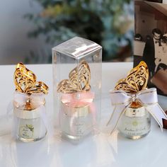 three small glass bottles with gold designs on the lids and bows tied around them, sitting on a table next to a book