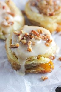 several pastries with icing and nuts on top of white wax paper lined up