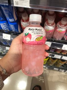 a person holding a bottle of liquid in front of a shelf full of sodas