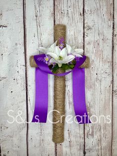 a cross decorated with flowers and purple ribbon on a white wooden background is the focal point for this photo