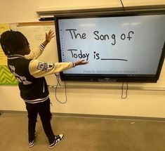 a young child standing in front of a large screen with the words the song of today is written on it