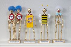 three golden skeleton figurines with blue hair and two yellow ones holding signs that say milk duds