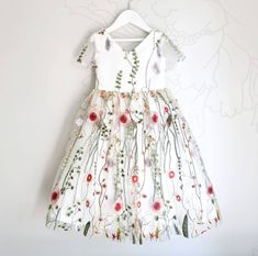 a white dress with red flowers on it hanging from a hanger against a wall