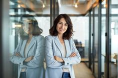 a woman standing in front of a glass wall with her arms crossed and looking at the camera