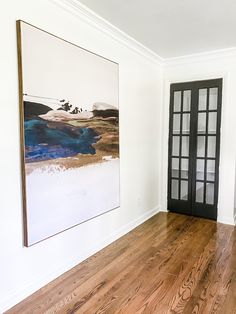 an empty room with wood flooring and large painting on the wall behind glass doors