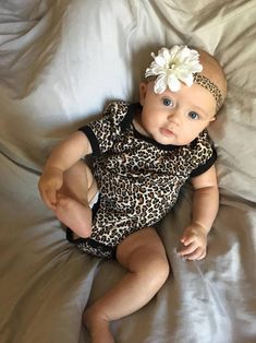 a baby laying on top of a bed wearing a leopard print romper and headband