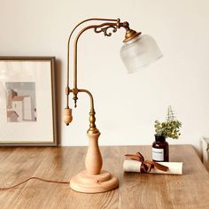 a desk lamp sitting on top of a wooden table next to a book and plant