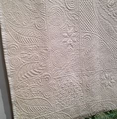 a white quilted wall hanging on the side of a building with green grass in front of it