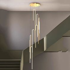 a modern chandelier hanging from the ceiling in a room with grey walls and stairs