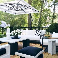 an outdoor living area with white furniture and black accents on the wooden deck, surrounded by greenery