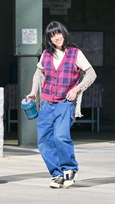 a woman is walking down the street with a bucket in her hand and wearing jeans