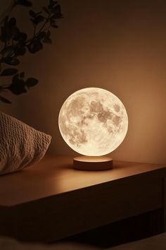 the moon lamp is sitting on a table next to a pillow and plant in front of it