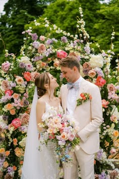 a bride and groom standing in front of a floral arch with flowers on it's sides