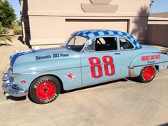 an old blue race car parked in front of a building with red rims and numbers on the side