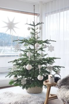 a small christmas tree with white balls and ornaments in a room next to a window