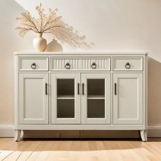 an empty room with a white cabinet and vase on the sideboard in front of it