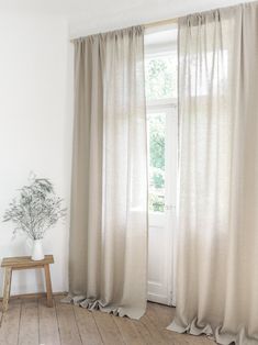 a living room with a wooden floor and white curtains on the window sill, next to a plant