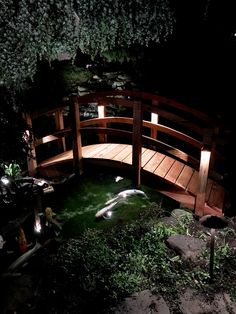 a small wooden bridge in the middle of a garden at night with lights on it