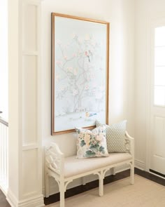 a white bench sitting in front of a painting on the wall next to a doorway