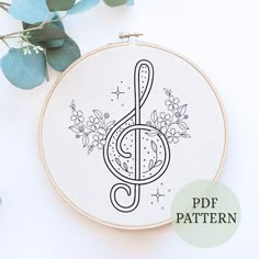 a cross stitch pattern with the letter g in black and white on a hoop next to eucalyptus leaves