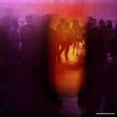 blurry photograph of people standing in front of a red and purple wall with an orange light