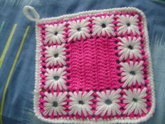 a pink and white crocheted square with flowers on the side, sitting on a bed