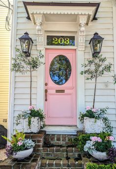 a pink front door with potted plants on the steps and two lights above it