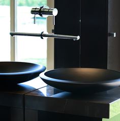 two black bowls sitting on top of a counter in front of a window with a faucet