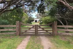 a wooden gate in the middle of a dirt road with trees and grass around it