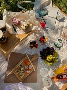 an outdoor picnic with food and drinks on the blanket in the grass, along with other items