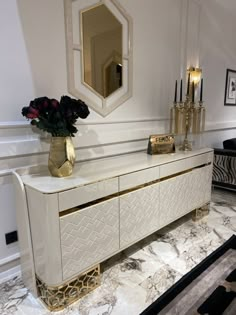 a white and gold console table with flowers on it in front of a wall mirror