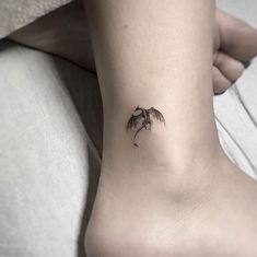 a small tattoo on the ankle of a woman's foot with a dragon flying above it