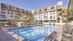 an outdoor swimming pool with lounge chairs and umbrellas next to the hotel's main building