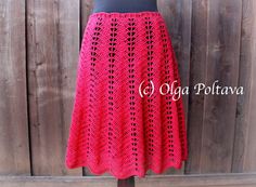 a red crocheted skirt on a mannequin head stand in front of a wooden fence