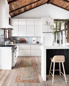 a kitchen with white cabinets and wooden floors, an area rug on the floor in front of the stove