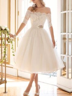 a woman in a white dress standing on a wooden floor next to a window with flowers