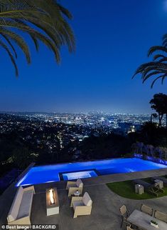 an outdoor swimming pool with lounge chairs and palm trees in the foreground at night