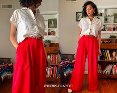 a woman standing in front of a bookshelf wearing red pants and a white shirt