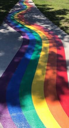 a long rainbow painted on the sidewalk in front of a tree and grass area with trees