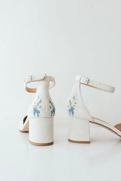 a pair of white high heeled shoes with blue flowers on the front and side