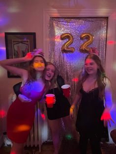 three women in costumes standing next to each other holding cups and posing for the camera