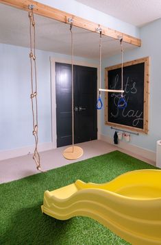 a child's playroom with swings, slide and chalkboard on the wall