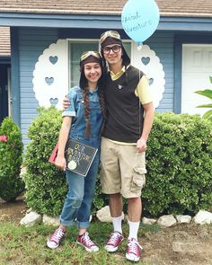 a man and woman standing in front of a blue house with a heart shaped balloon