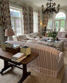 a living room filled with lots of furniture next to two windows and a chandelier